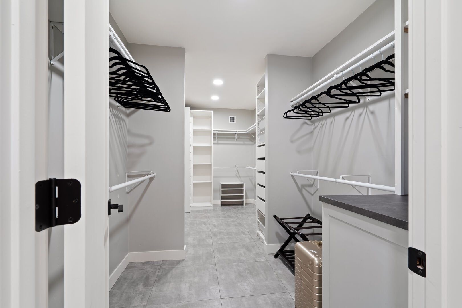 Un pasillo estrecho con paredes blancas, suelo de baldosas grises y un mueble de almacenamiento central con varios compartimentos.