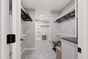 A narrow hallway with white walls, grey tiled flooring, and a central shelving unit with multiple compartments.