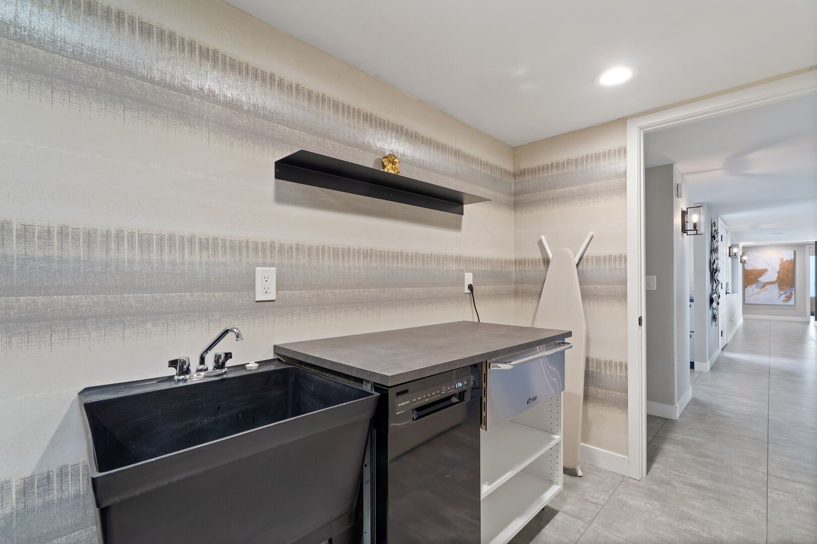 A modern kitchen with a built-in dishwasher, a countertop with a sink, and a wall-mounted shelf.