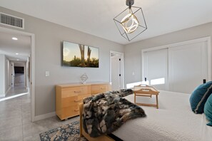 Un dormitorio con cama, cómoda, escritorio, silla, alfombra y lámpara en el techo.