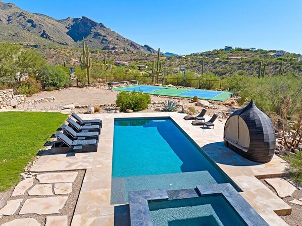 A swimming pool with a stone deck, lounge chairs, and a covered seating area.