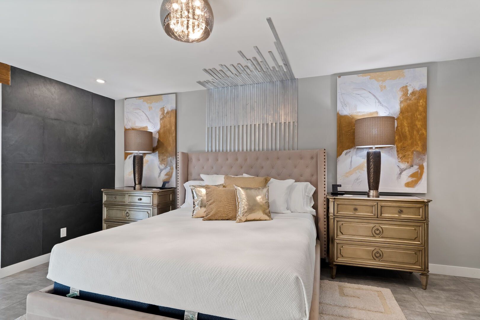 Un dormitorio moderno con una cama grande, dos mesitas de noche, un candelabro, arte abstracto en la pared y una pared con textura.