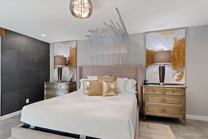 A modern bedroom with a large bed, two bedside tables, a chandelier, abstract wall art, and a textured wall.