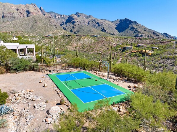 Una cancha de baloncesto con montañas al fondo, rodeada de cactus y vegetación escasa.