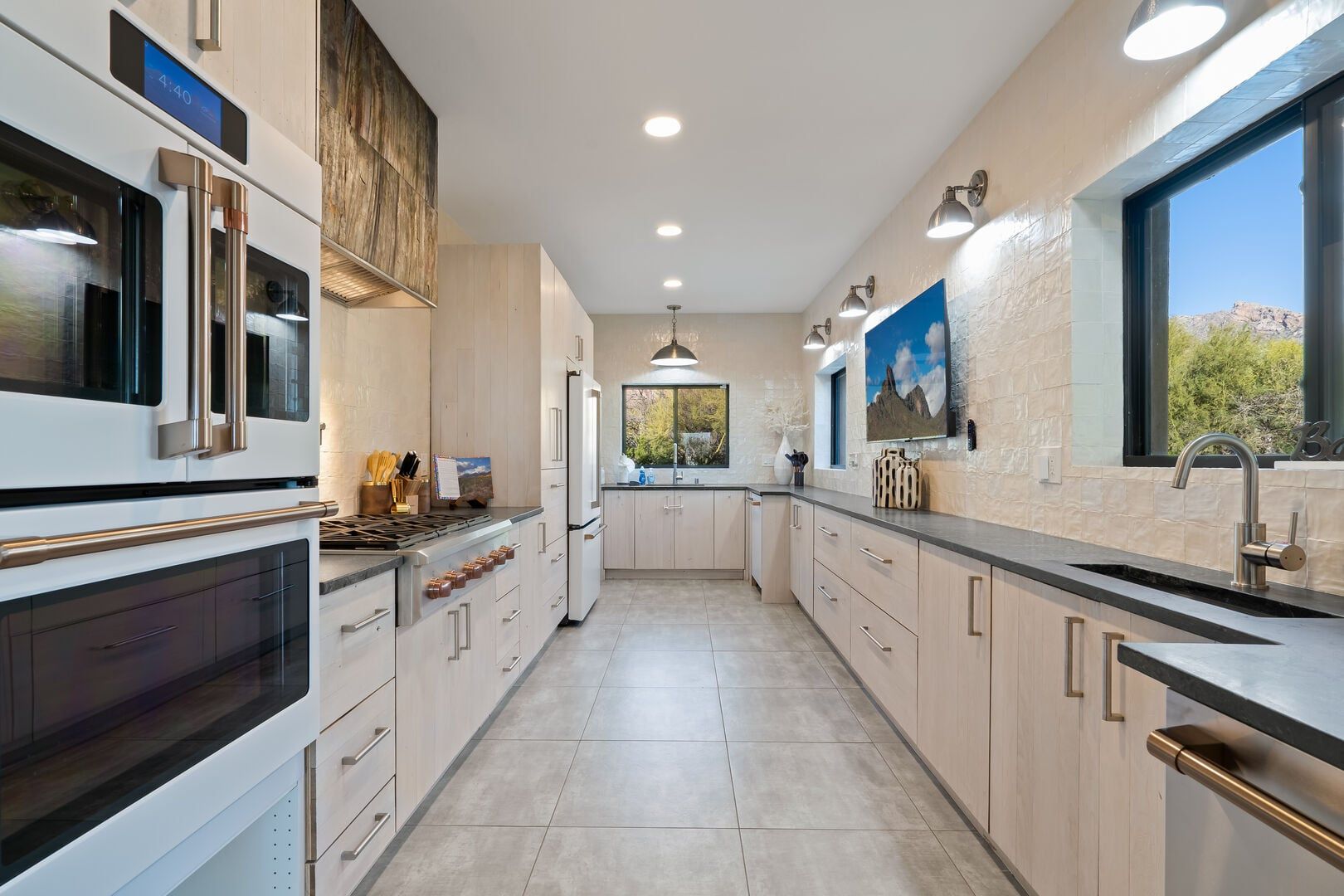A modern kitchen with stainless steel appliances, light wood cabinetry, and a large window providing a view of the outdoors.