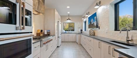 A modern kitchen with stainless steel appliances, light wood cabinetry, and a large window providing a view of the outdoors.