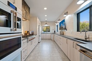 A modern kitchen with stainless steel appliances, light wood cabinetry, and a large window providing a view of the outdoors.