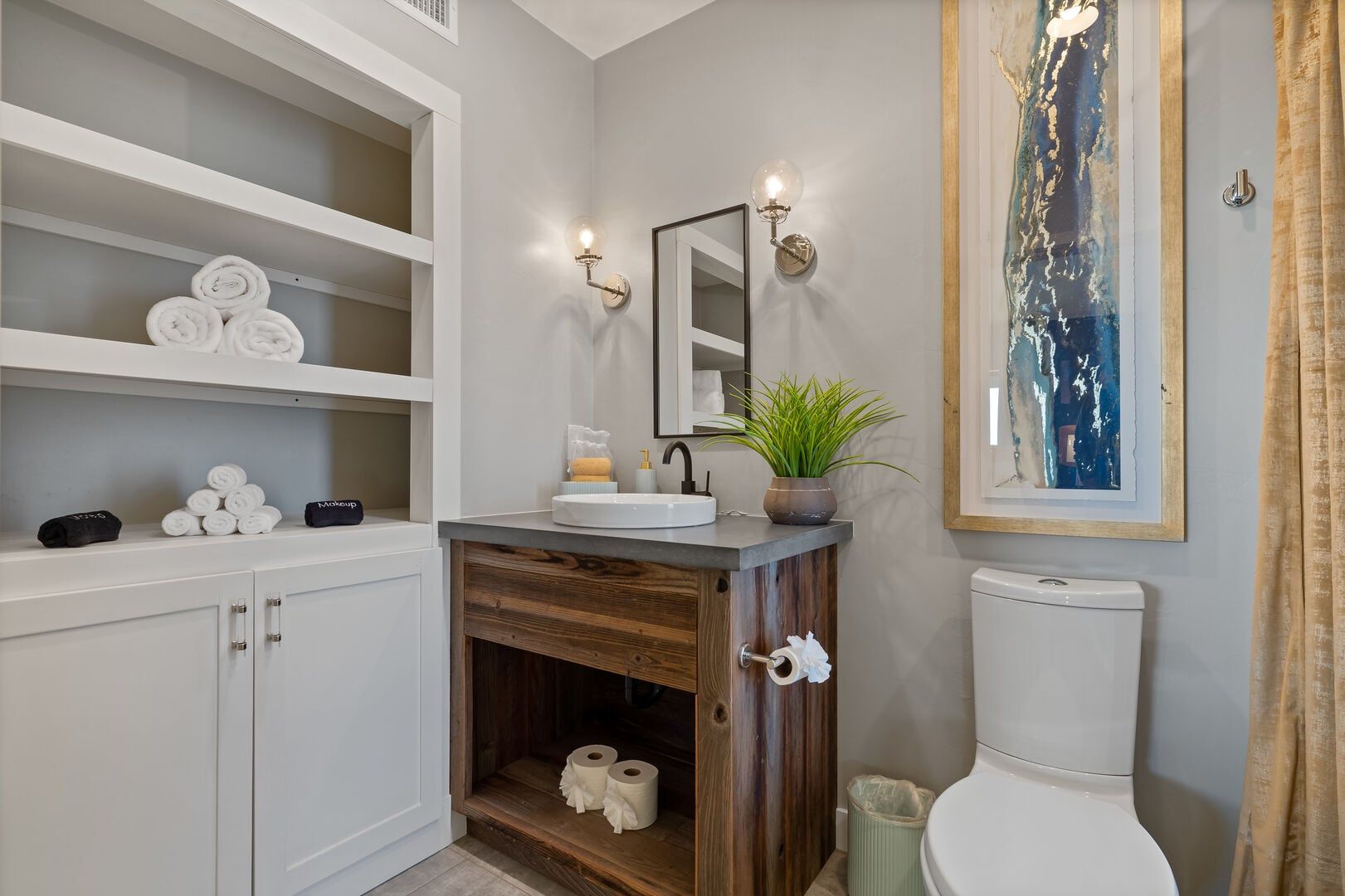 A bathroom with a white toilet, a wooden vanity with a sink, a mirror, and a shelf with towels.