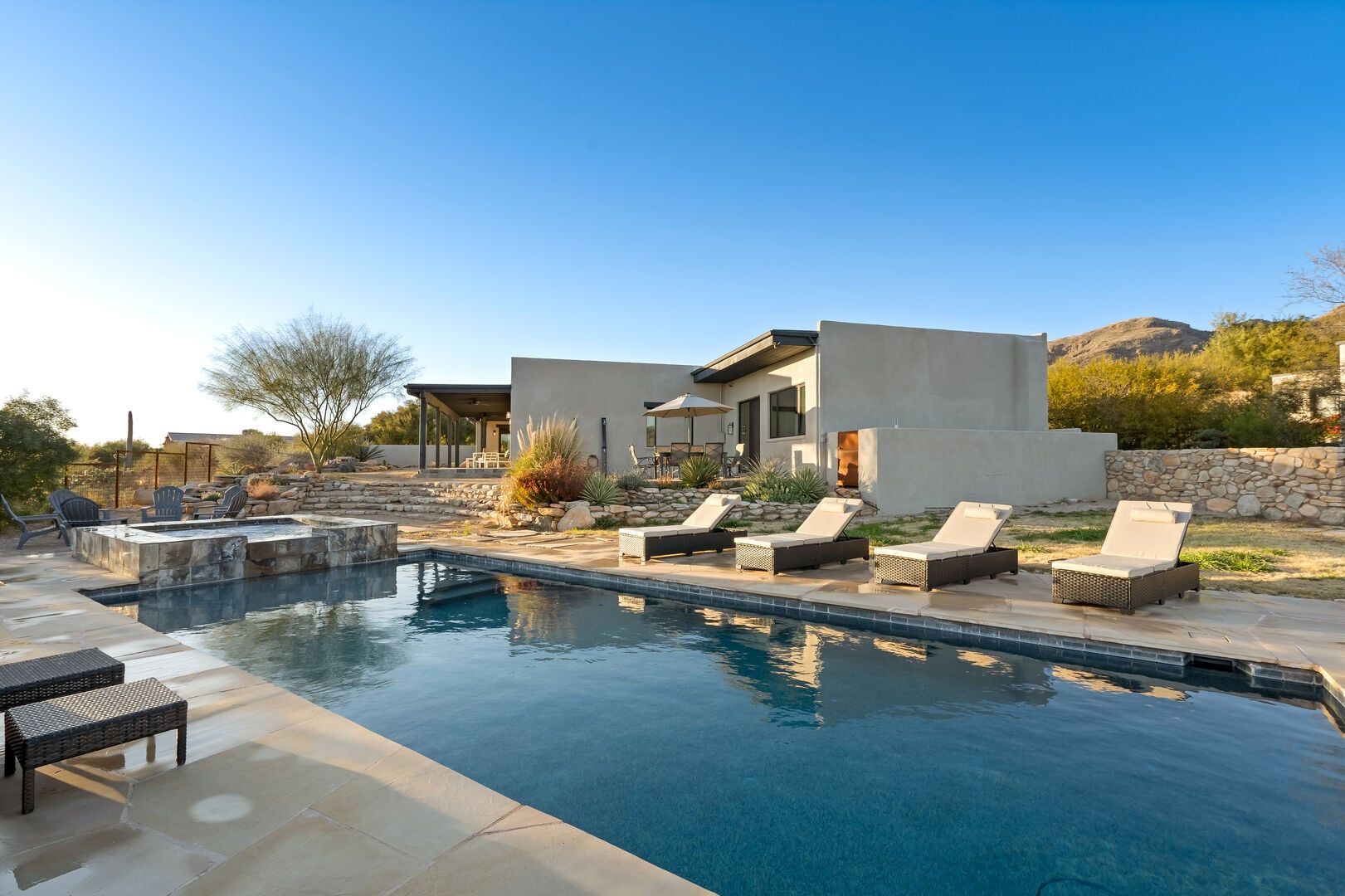 A modern house with a swimming pool, outdoor seating, and a stone wall.