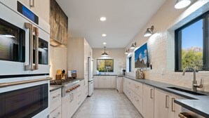 Une cuisine moderne dotée d’appareils électroménagers en acier inoxydable, de meubles de rangement en bois clair et d’une grande fenêtre offrant une vue sur l’extérieur.