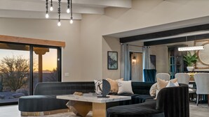 Un salon moderne doté d’une grande fenêtre, d’un canapé noir, d’une table basse en marbre et d’un coin repas avec des chaises.