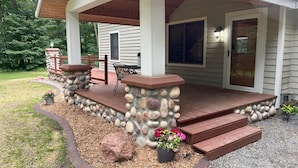 A covered porch with stone pillars, a wooden deck, and a stone wall.