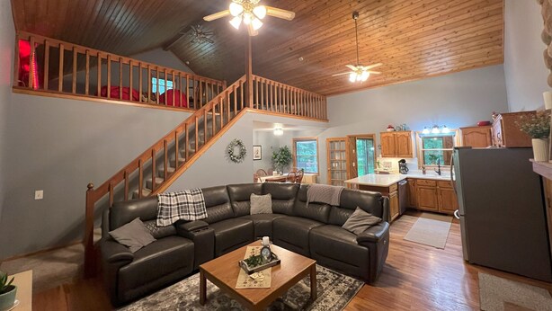 A spacious living area with a wooden ceiling, a black leather sectional sofa, a wooden coffee table, and a kitchen in the background.