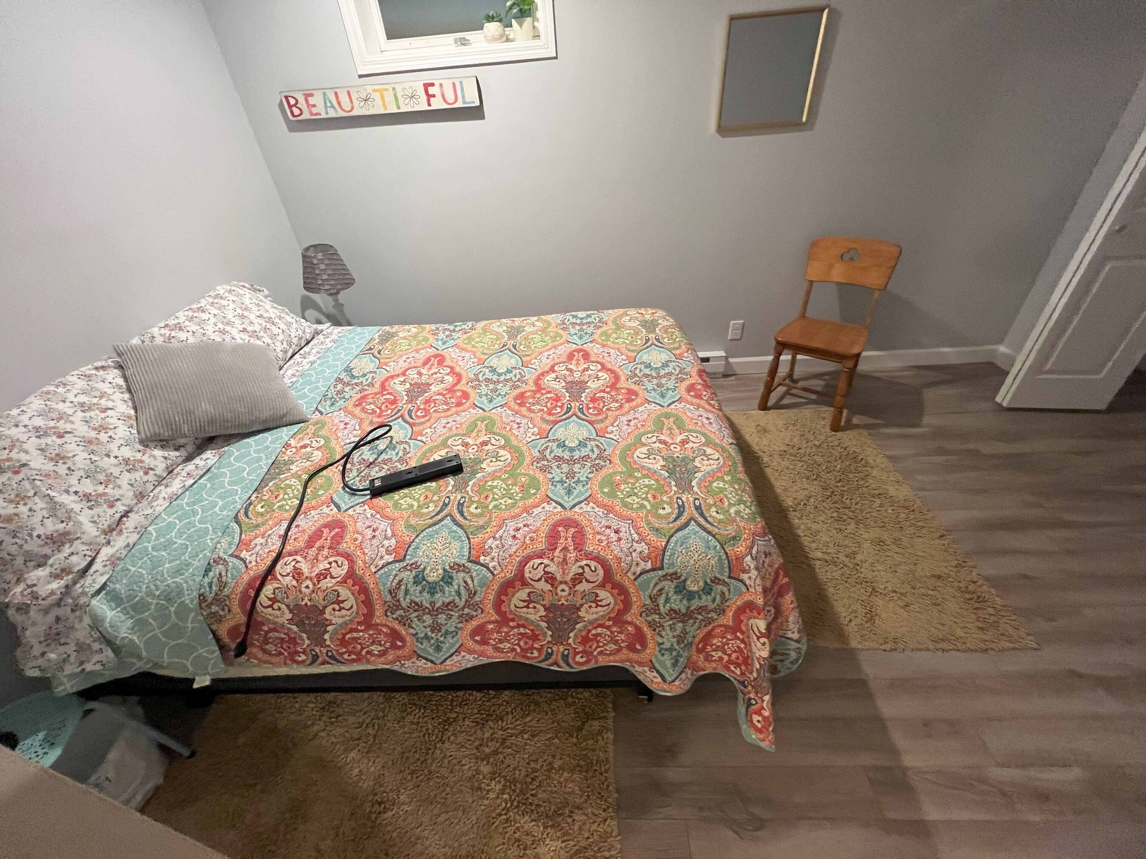 A bedroom with a bed, a chair, a rug, and a wall sign.