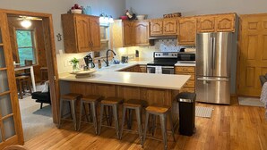 A kitchen with wooden cabinets, a stainless steel refrigerator, a sink, and a bar stool area.