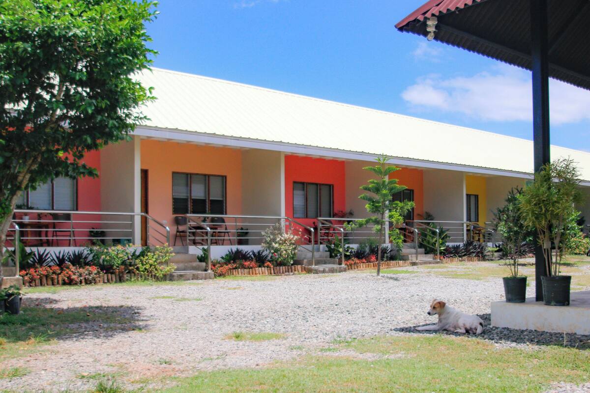 A building with a covered entrance, outdoor seating, and a paved area with gravel and grass.