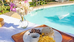 Ein Esstisch mit einer Speisenplatte, einer Kaffeetasse und einem Blumenstrauß am Pool.