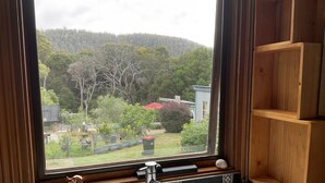 A bathroom with a white sink, a wooden shelf, and a window overlooking a garden and hills. - A cosy garden cottage, just 400m to the surf beach. (Bicheno)
