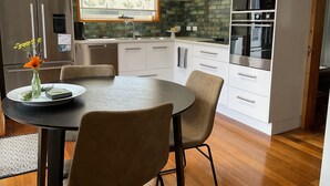 A modern kitchen with white cabinets, a built-in oven, and a window with a leaf-patterned blind. - A cosy garden cottage, just 400m to the surf beach. (Bicheno)