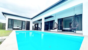 A modern house with a swimming pool, large windows, and a hanging chair. - Paradise Villas (Nadi)