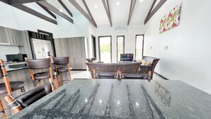 A modern kitchen with dark countertops, wooden chairs, and a central island. - Paradise Villas (Nadi)