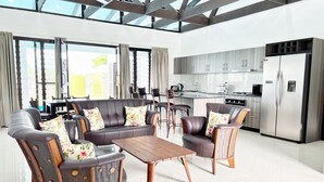 A modern living room with a sofa and chairs, a wooden coffee table, and a kitchen area with a refrigerator and stove. - Paradise Villas (Nadi)