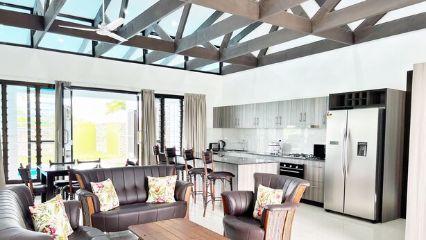 A modern kitchen with stainless steel appliances, a dining area with leather sofas and chairs, and large windows allowing natural light. - Paradise Villas (Nadi)