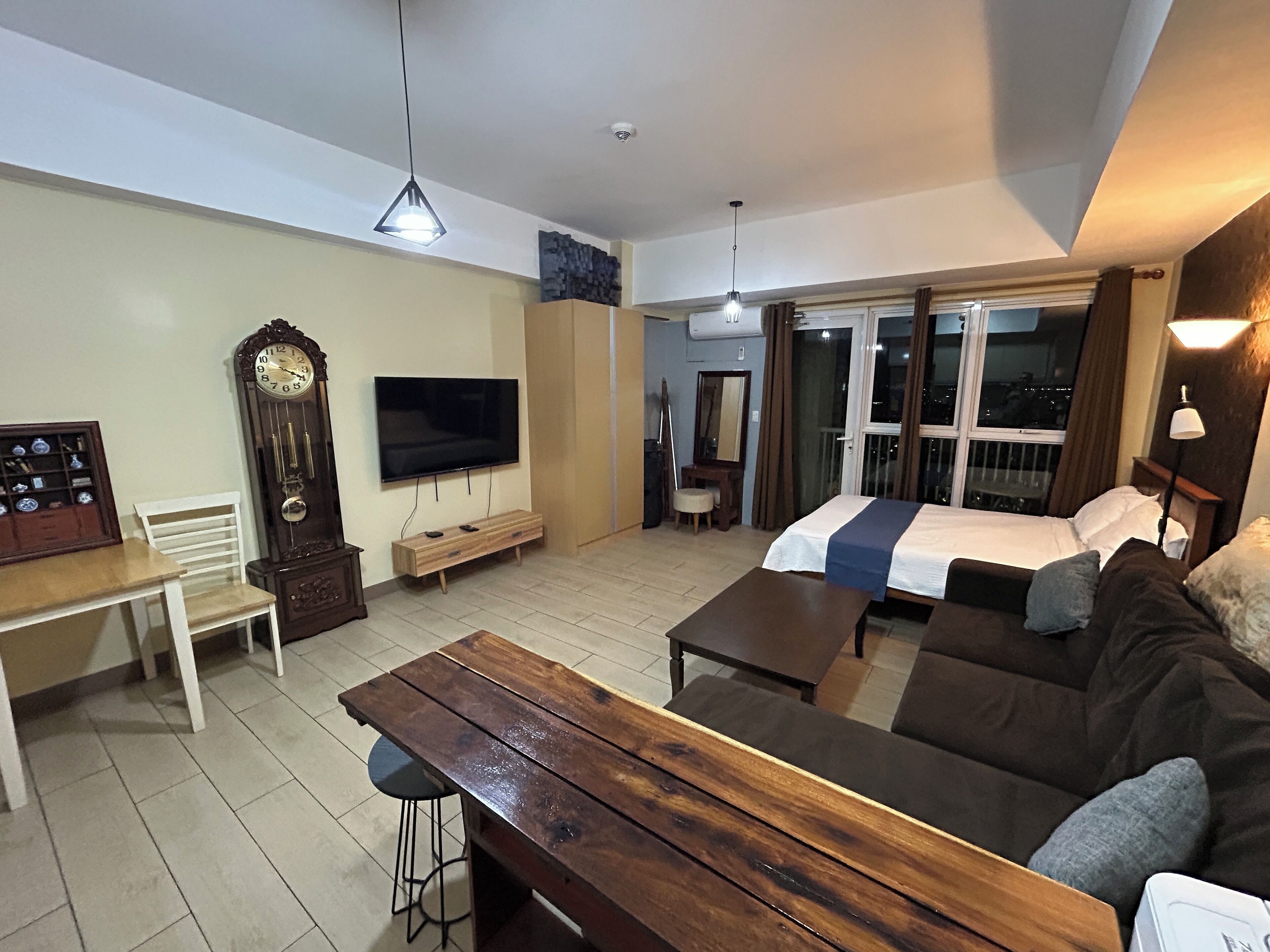 A modern living room with a large TV, a wooden coffee table, a sofa, and a dining area with a white chair and a wooden cabinet.