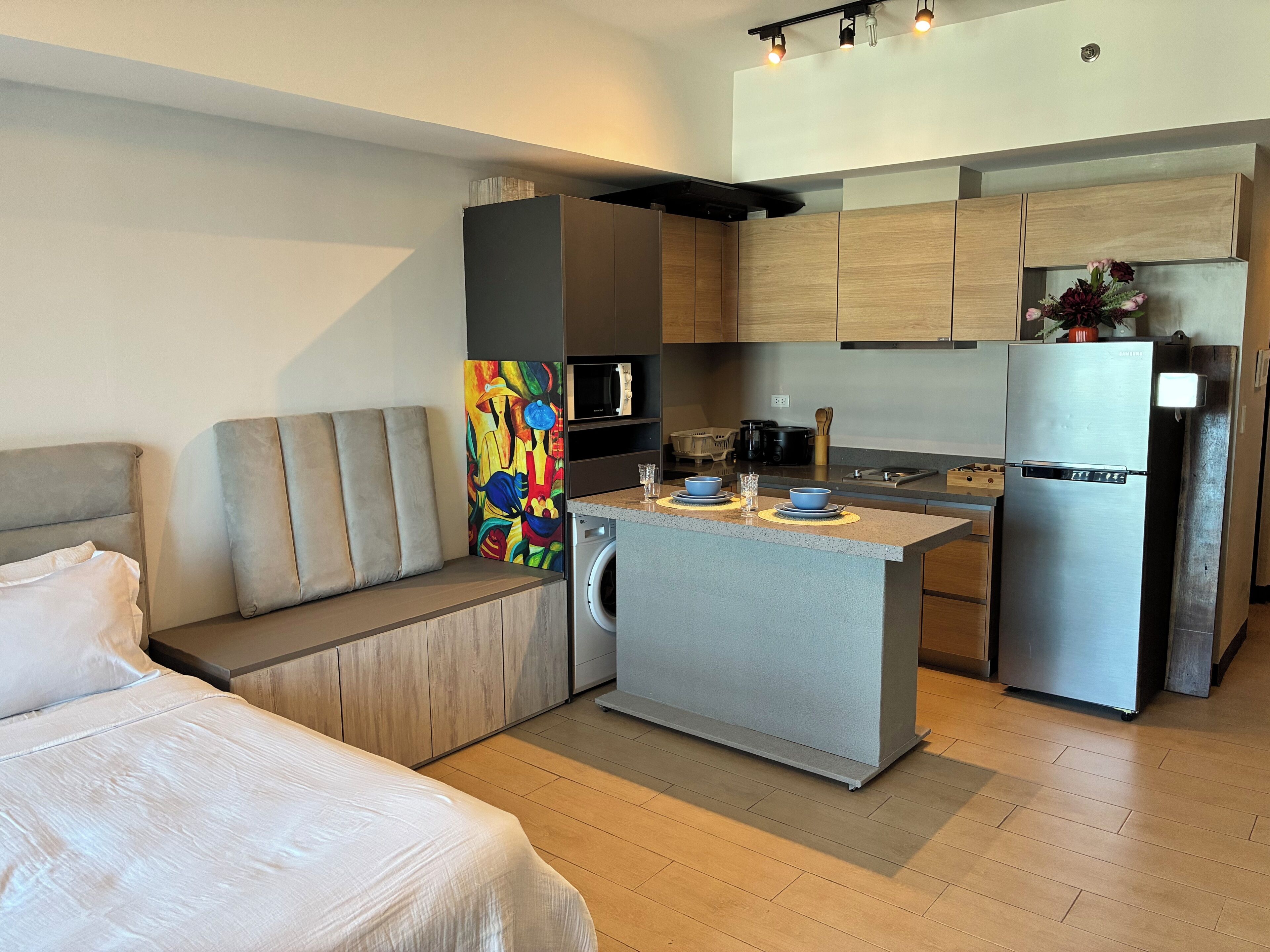 A compact kitchenette with a built-in microwave, a stainless steel refrigerator, and a small island with a sink.