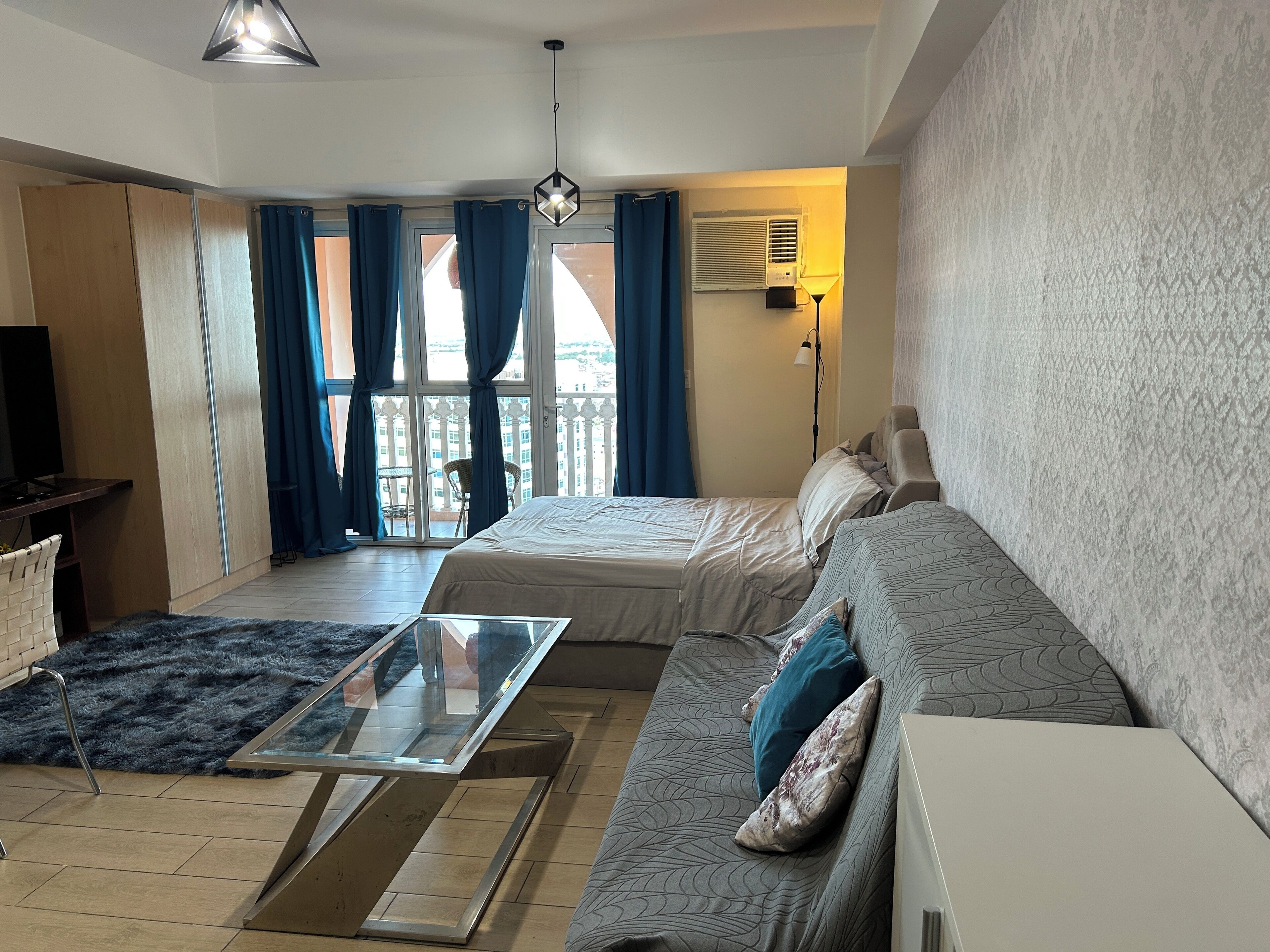 A modern bedroom with a bed, a sofa, a glass coffee table, and a TV.