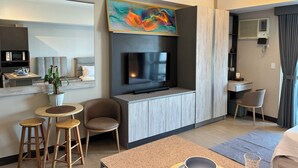 A modern hotel room with a flat-screen TV, a dining area with stools, a small table, and a potted plant. - VenizLex  (Taguig)
