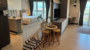 A hotel room with a bed, a TV, a dining area with a table and chairs, and a balcony with a view. - VenizLex  (Taguig)