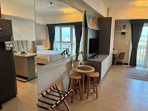 A hotel room with a bed, a TV, a dining area with a table and chairs, and a balcony with a view.