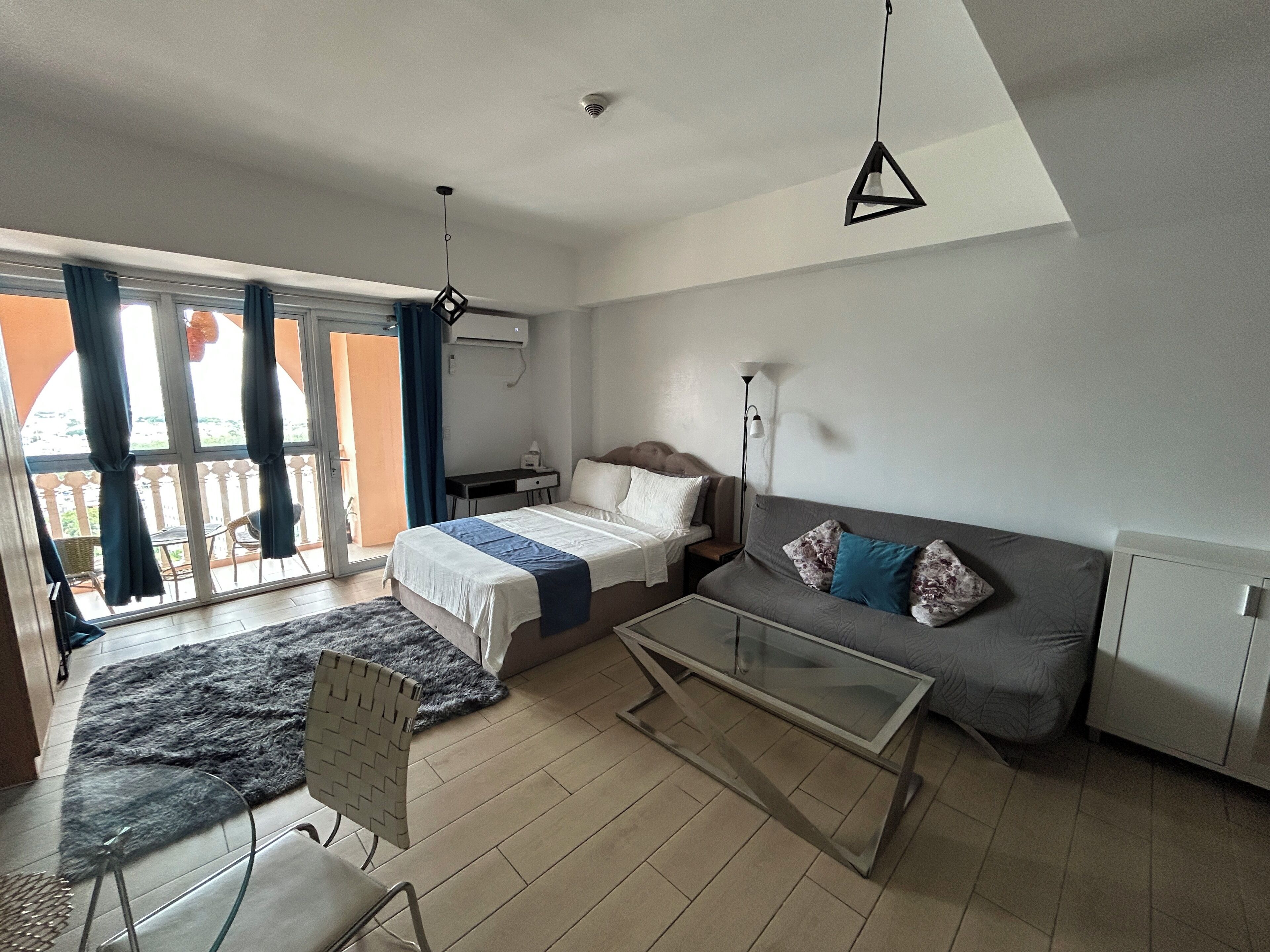 Une chambre moderne avec un lit, un canapé, une table basse en verre et une vue sur l’extérieur.