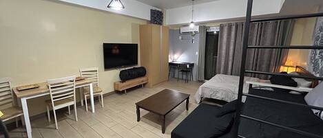 A compact living space with a TV, a small dining table, a sofa, and a bunk bed.