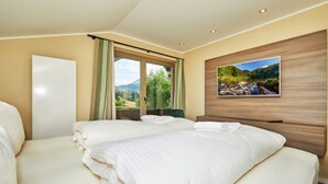 Una camera d'albergo con due letti, un'ampia finestra vista su vegetazione e montagne, e un televisore a parete.