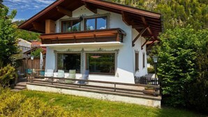 Un chalet a due piani con un balcone, ampie finestre e un terrazza in legno.