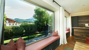 Un interno moderno con un'ampia finestra, un angolo salotto con cuscini, un tavolo in legno e un piano cucina.