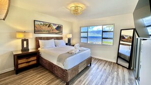 Ein Schlafzimmer mit einem großen Bett, einem Nachttisch, einer Lampe, einem Gemälde, einem Fenster mit Blick und einem Fernseher.