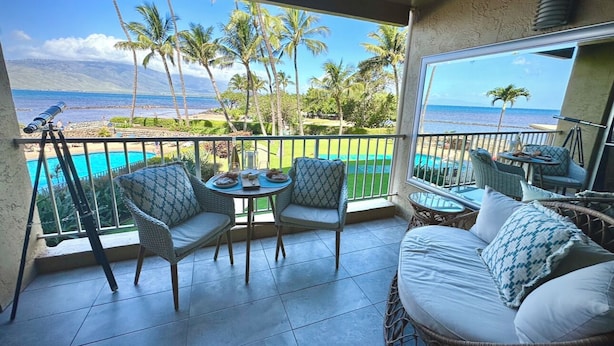 Ein Balkon mit Korbmöbeln, einem Tisch und Blick auf Strand und Palmen.