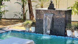 A pool with a waterfall feature, surrounded by potted plants and a statue. - Private Beach Front Villa (Thalikulam)