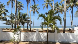 A sandy beach with palm trees and a white wall in the foreground. - Private Beach Front Villa (Thalikulam)