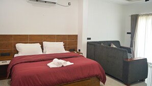 A hotel room with a bed, a grey sofa, a wooden headboard, an air conditioning unit, and a ceiling fan. - Private Beach Front Villa (Thalikulam)