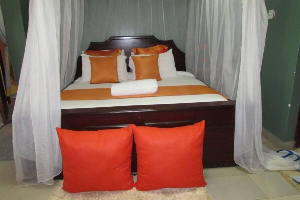 A bed with a canopy, two orange pillows, and a white blanket.