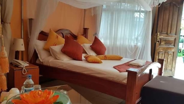 Een bed met hemel, een nachtkastje met lamp, en een decoratieve schaal op de vloer.