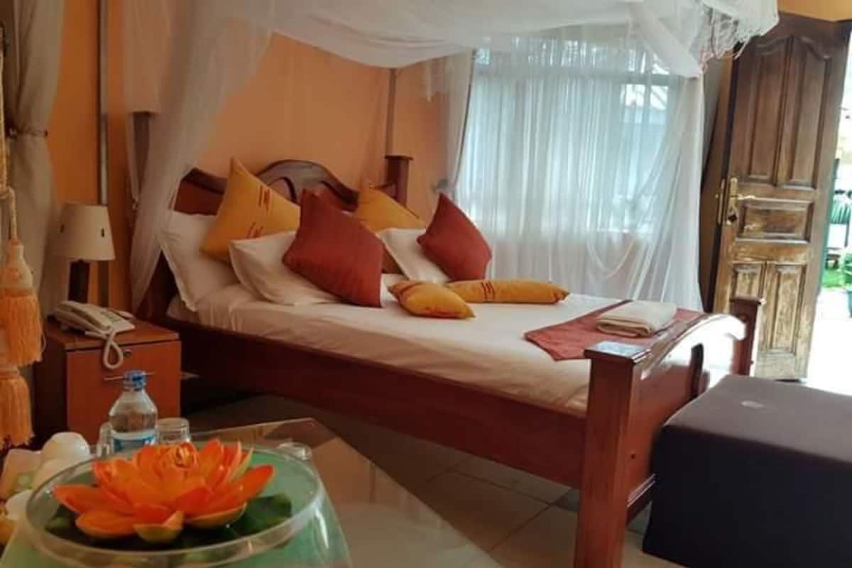 A bed with a canopy, a bedside table with a lamp, and a decorative bowl on the floor.