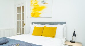 Relax in a serene bedroom with a neatly made bed, grey headboard, and a large abstract painting.