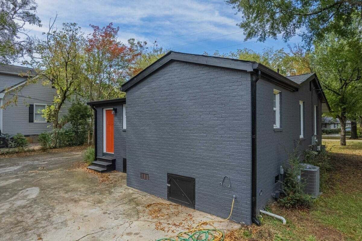 A small, single-story building with a dark gray exterior and a bright orange door.