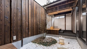 Un jardin de style japonais traditionnel, avec une clôture en bois, un petit arbre, des galets blancs et une lanterne.