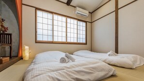 Une chambre d’hôtel avec deux lits, une grande fenêtre et un sol recouvert de tatamis, dans le style traditionnel japonais.